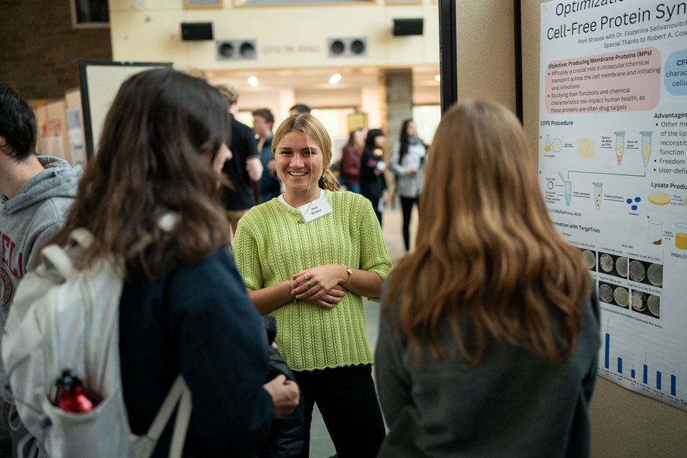 Student talks with onlookers about Cell-Free Protein related poster presentation