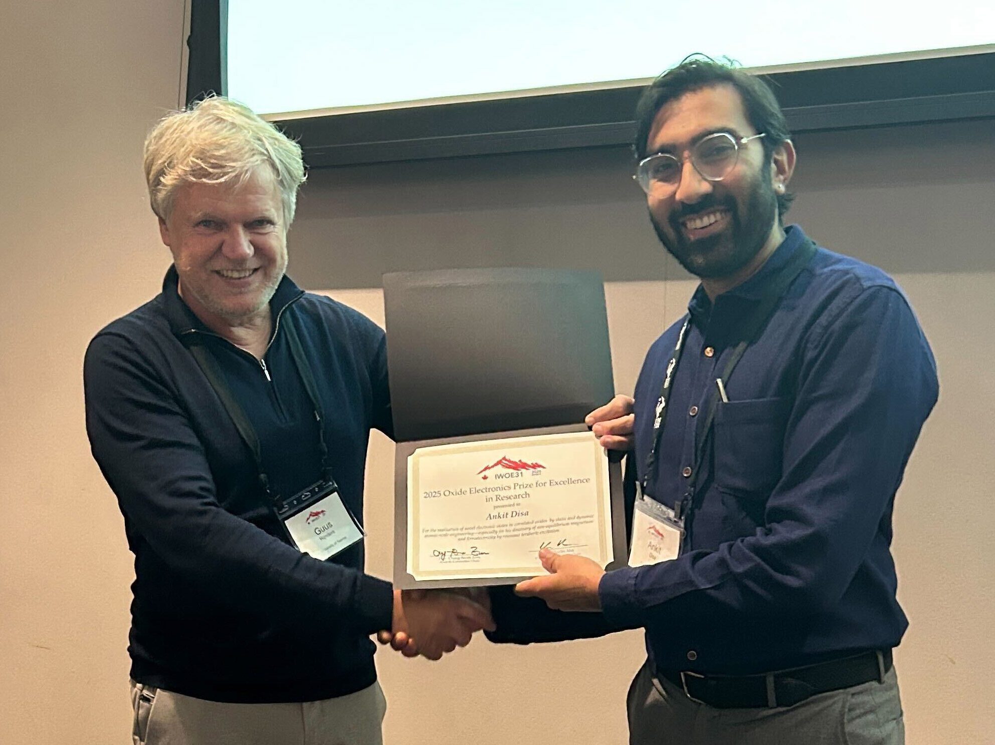 Two men hold a folder that contains a certificate. Ankit Disa is on the right. 