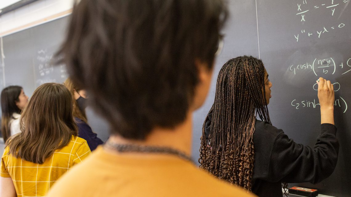 student chalks an equation onto a blackboard