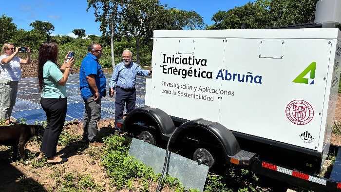 Four people stand to the left of a large whiite box on wheels. These words in Spanish are written on the side of the box: 