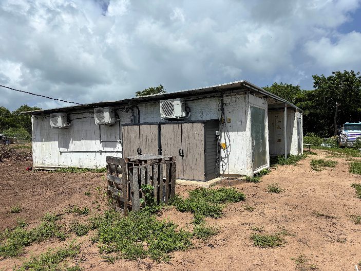 Two white shipping containers are side by side and joined by a roof.