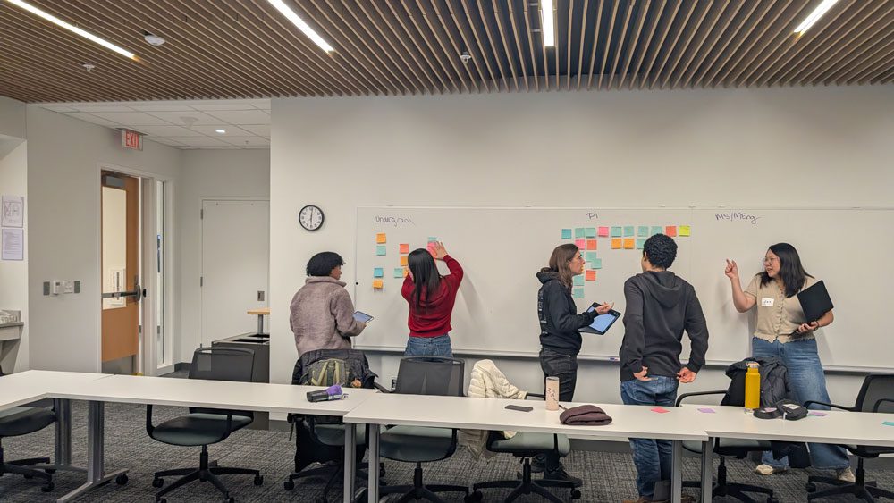 Students talk and work together at whiteboard with sticky notes