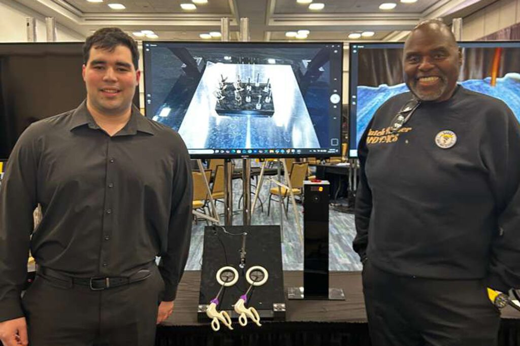 Two men stand with a computer screen between them at a conference.