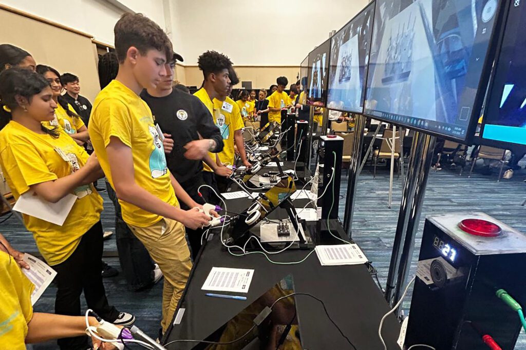 Students lined up in front of computer screens practice using surgical tools