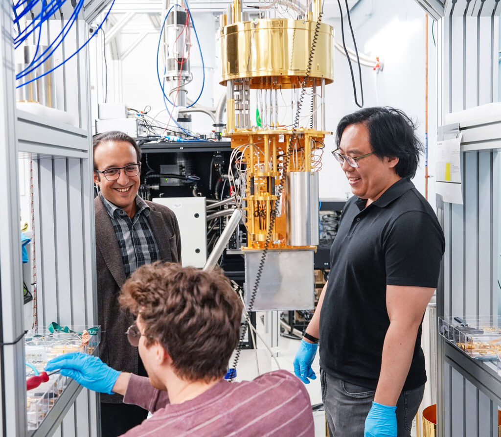 Three men stand around an open cryostat.