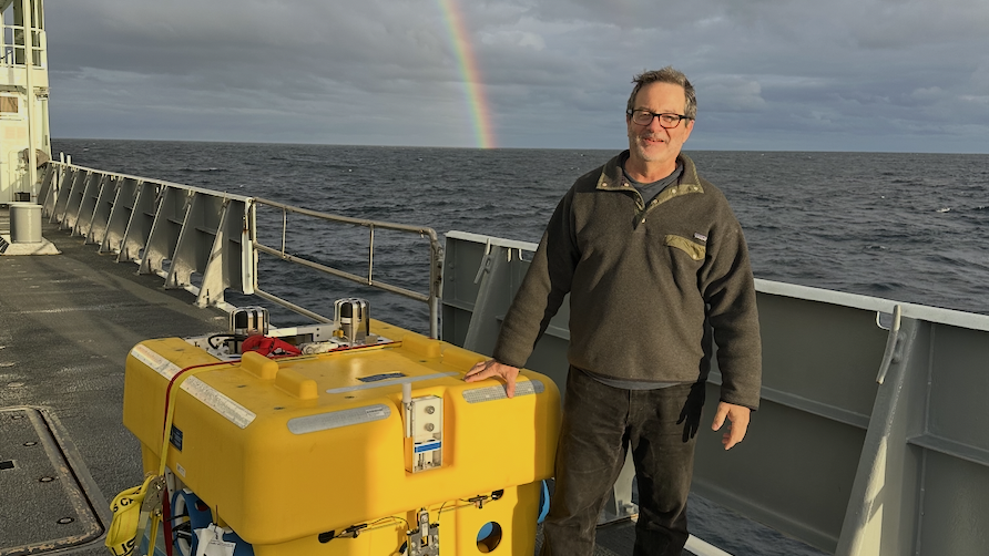 EAS Faculty member Geoff Abers on the deck of a research vessel as he prepares to deploy a bright yellow seismometer on the ocean floor near New Zealand.