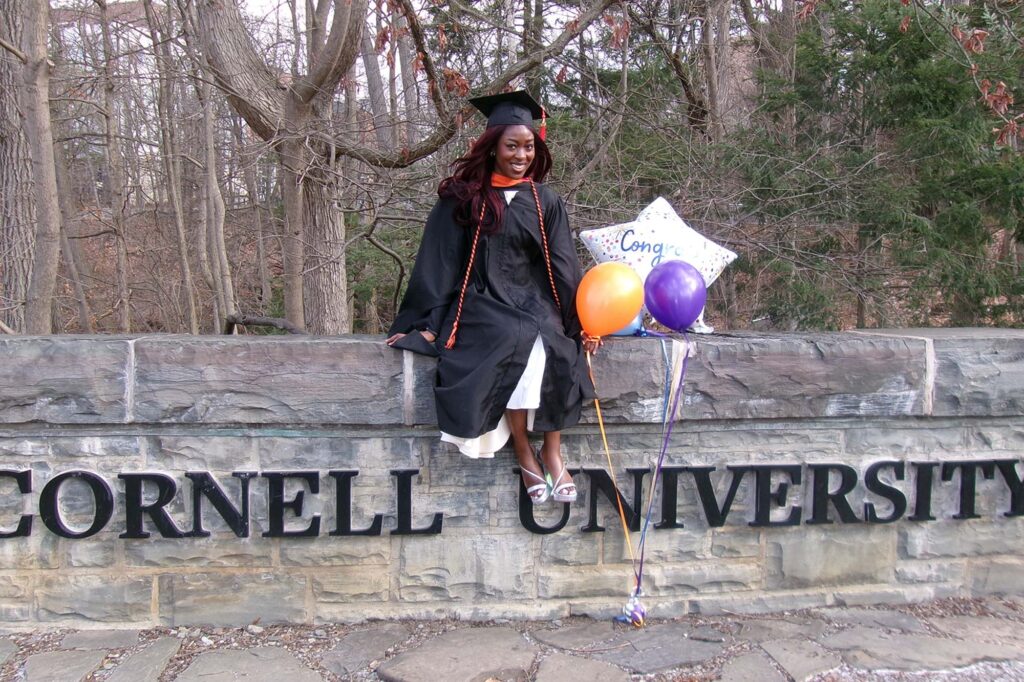 MEng graduate Sophia Ayeni sits on stone wall in graduation regalia with balloons on graduation day.